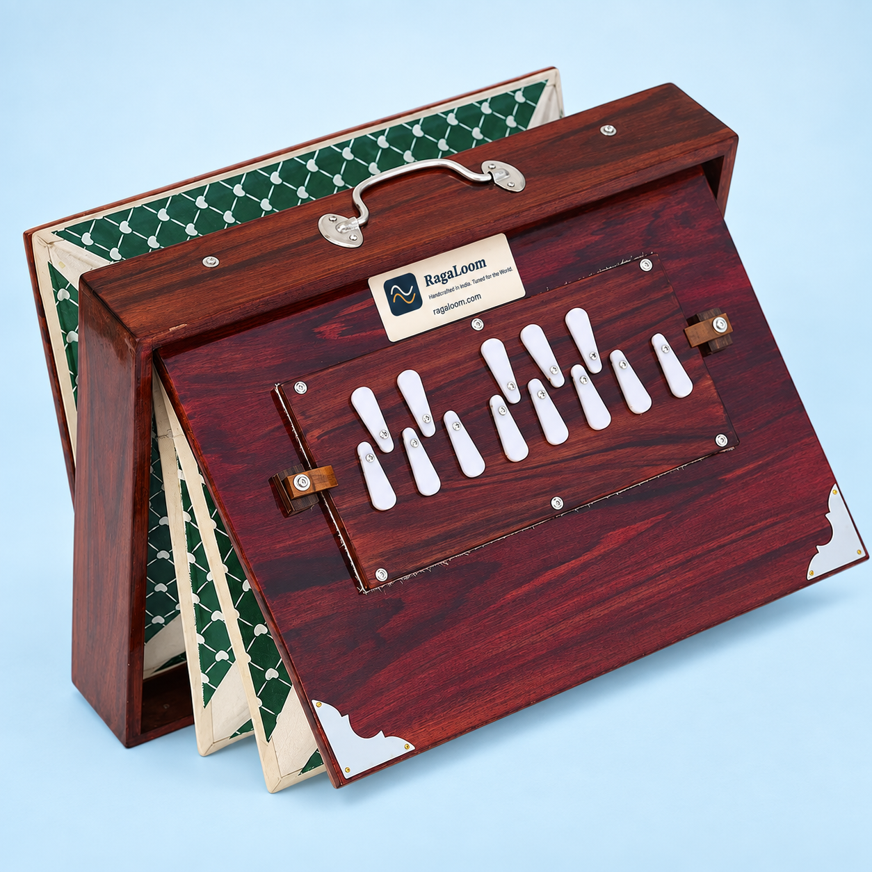Cherry-finish shruti box with green patterned bellows open, left angle on pale blue background
