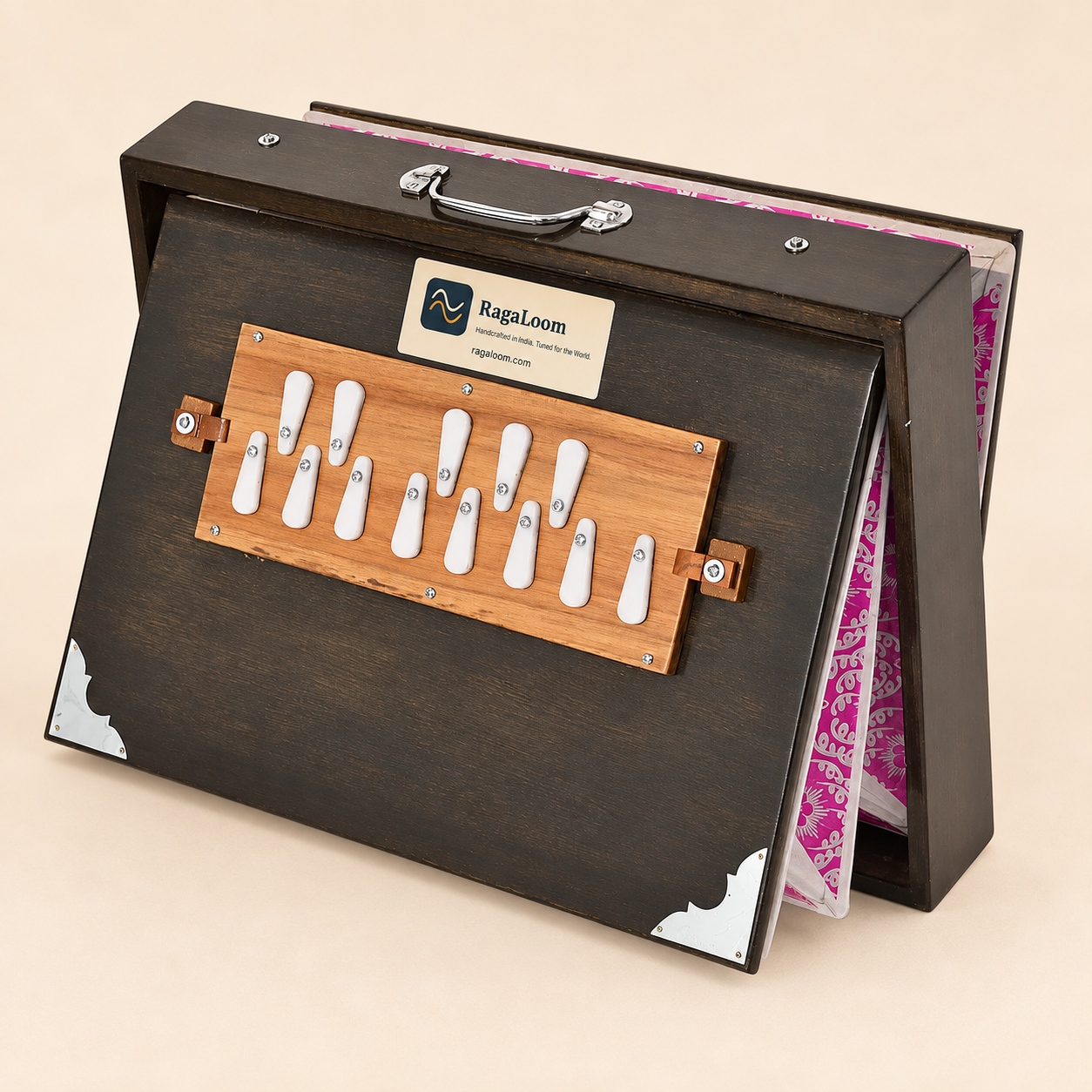 Oak-finish shruti box with patterned magenta bellows open, front angle on warm sand background