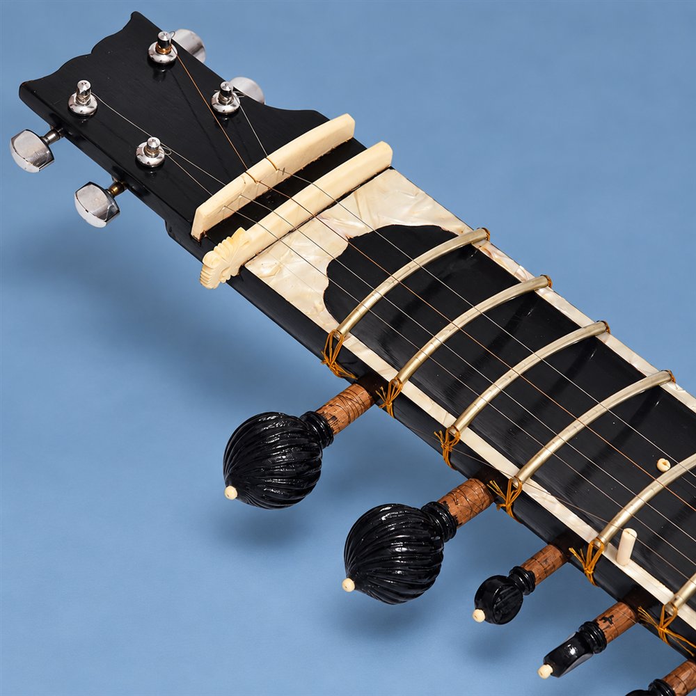 Black traveler sitar showing tuning pegs and curved frets
